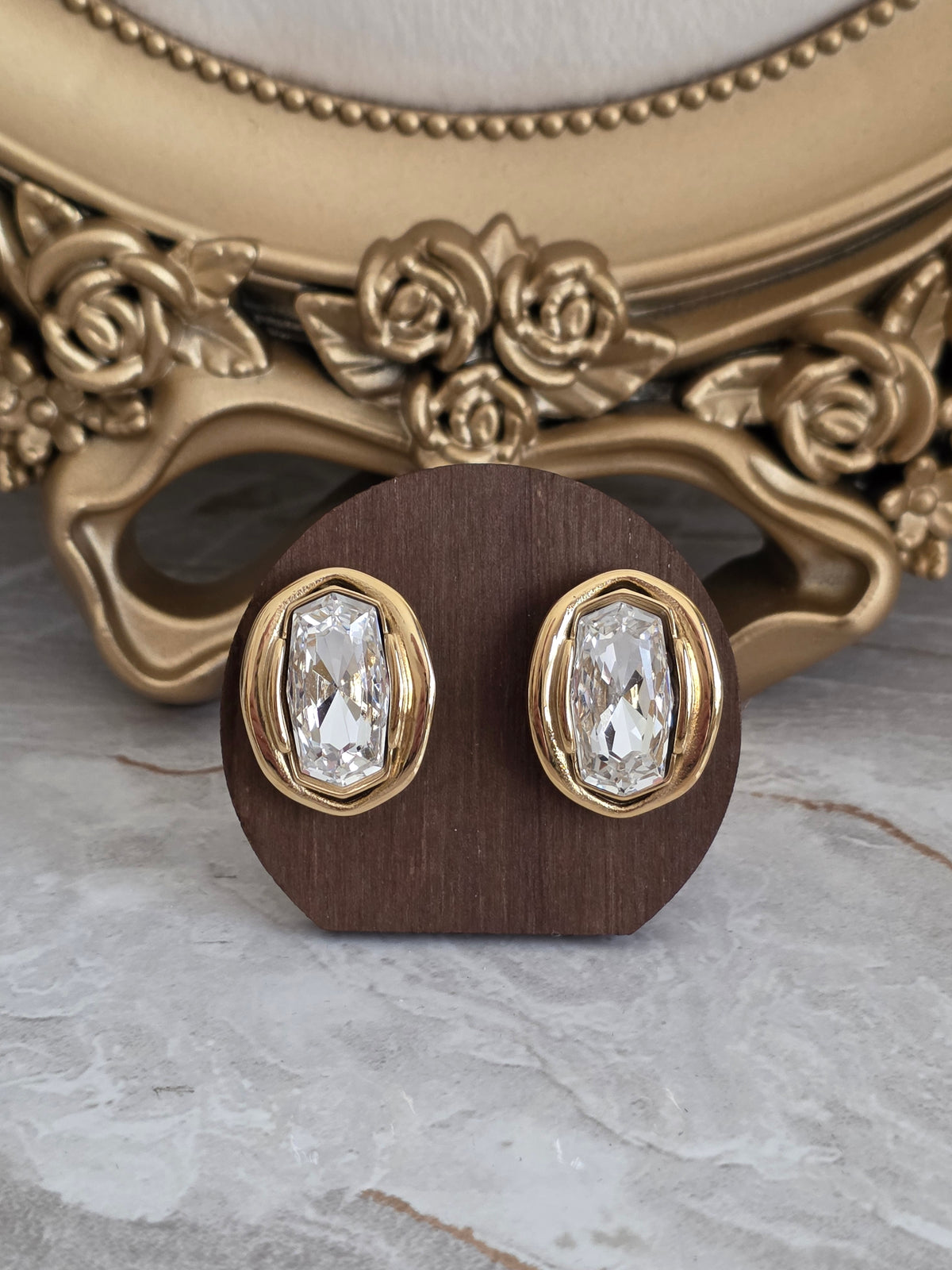 Oya Earrings featuring a faceted clear glass stone in a sculptural gold-tone oval setting.