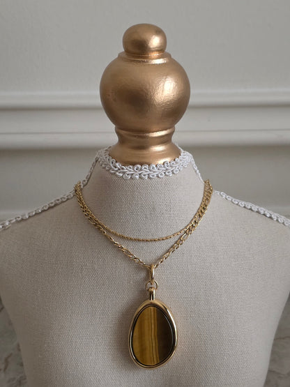 Layered gold necklace with two chains and a teardrop-shaped Tiger’s Eye gemstone pendant displayed on a mannequin bust.