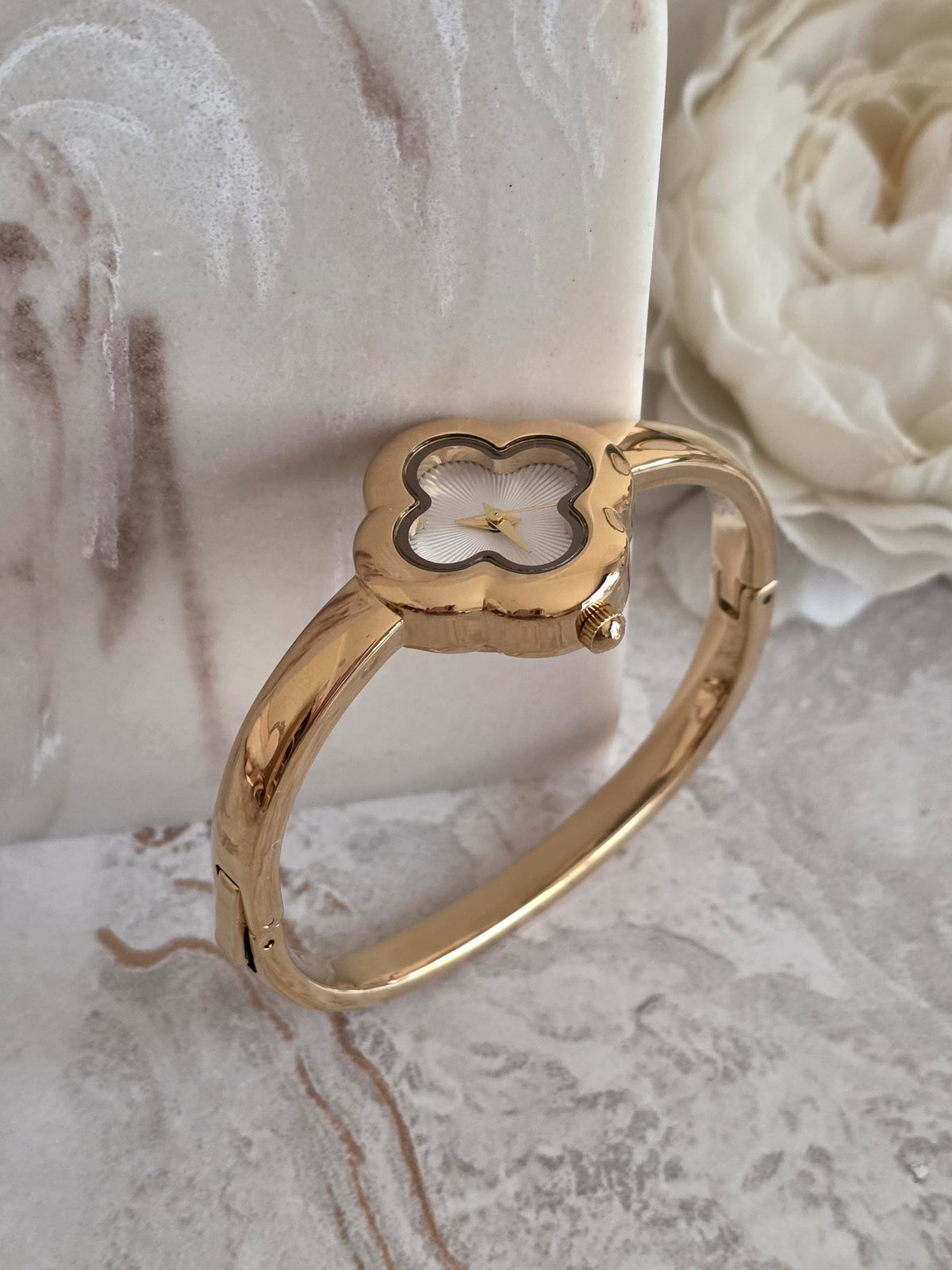 Gold bangle watch featuring a delicate four-leaf clover-shaped face, textured white dial and polished gold-tone bracelet design.