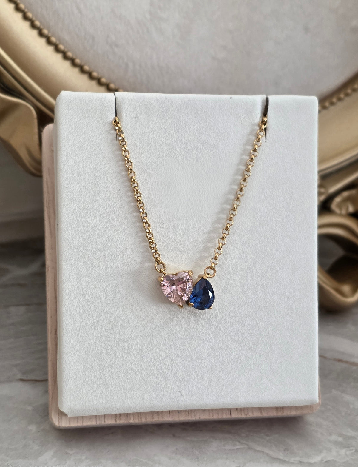 Lilay Necklace with pink heart and blue teardrop stones on a delicate gold chain.