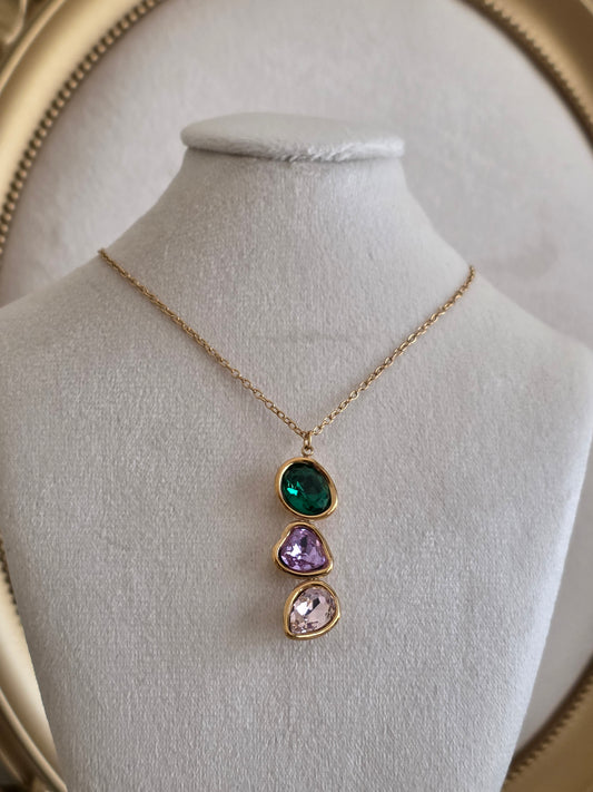 Gold-tone pendant necklace featuring three stacked crystal stones in emerald green, purple and soft pink on a delicate chain.