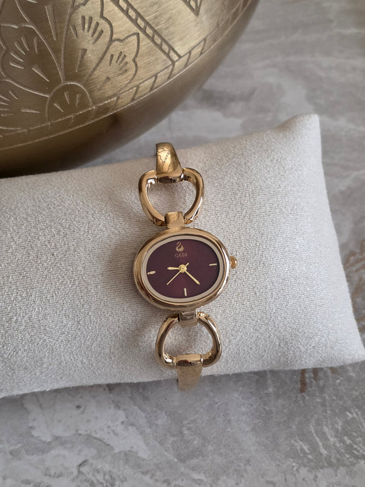 Rina Watch featuring a burgundy dial, gold-tone rounded-square face and elegant open-link stainless steel bracelet with gold plating.