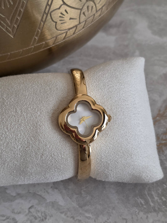 Gold bangle watch featuring a delicate four-leaf clover-shaped face, textured white dial and polished gold-tone bracelet design.