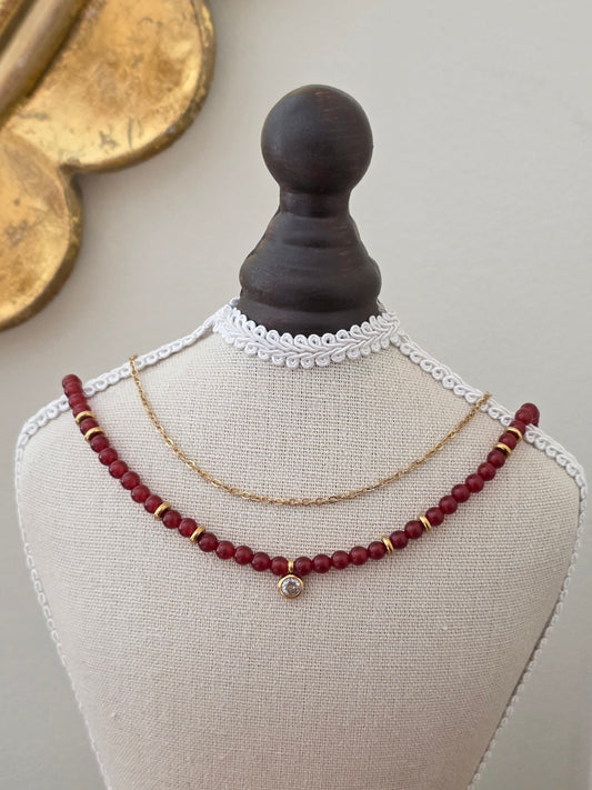 Feyza double-chain necklace featuring a delicate gold-tone chain, burgundy-red beads, gold accents and a sparkling crystal charm.