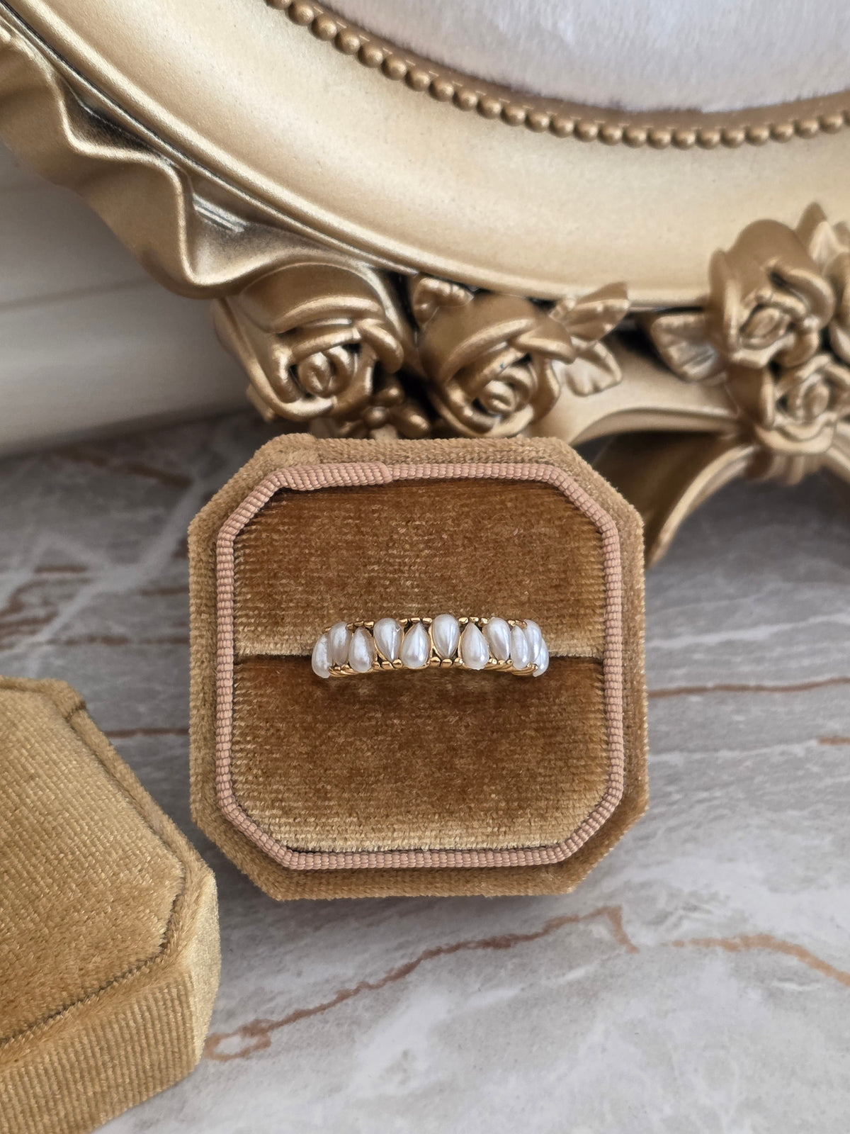 Eldana Pearl Ring featuring simulated white pearls with delicate gold detailing, displayed in a beige velvet jewellery box.